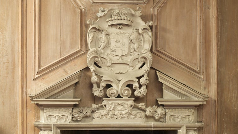 Details of a stone coat of arms on oak panelling over fireplace